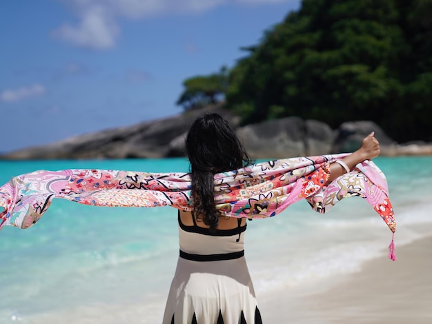 Back of woman open arms looking at view on white sand beach and clear blue sea on island