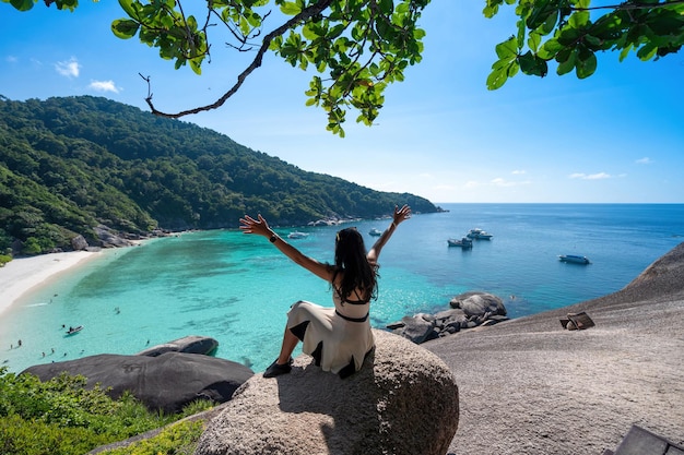 Back of woman tourist sitting on viewpoint sailing rock on Similan island watching at beautiful seascape view with clear blue sky in Phuket Thailand girl has happy vacation Travel concept