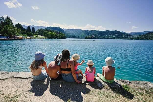 Back of woman with five kids sit in pier of view beautiful Bled Lake Slovenia Mother of many children