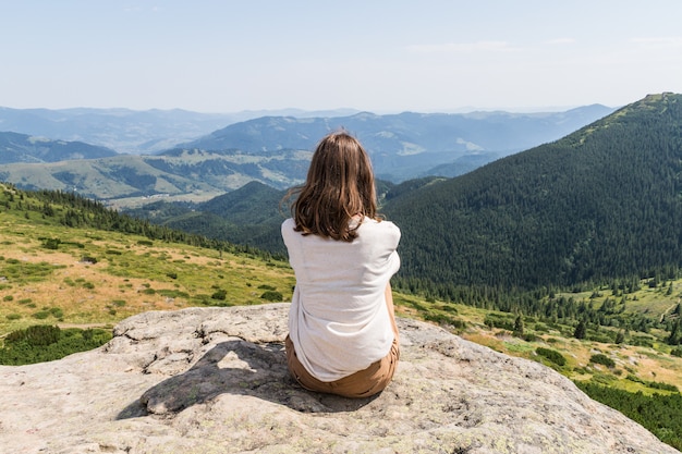 Back of young female person sitting on top of the rock in ukrainian carpathian mountains