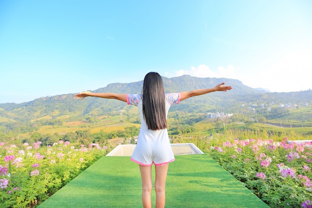 Back of young woman feeling free with arms wide open at beautiful trees and mountains on b