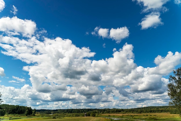 Background of a blue sky with clouds a green field river and forest