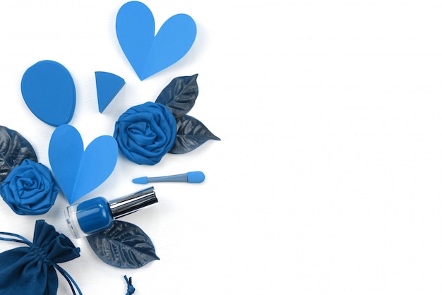 Background of decorative cosmetics in blue on white. concept of Valentine's day composition is flat lying lipstick flower heart leaf nail Polish