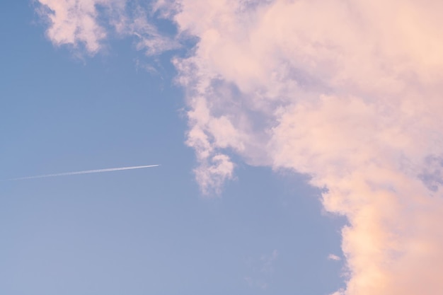 Background image of blue bright sky with pastel pink and white clouds and airplane with trail