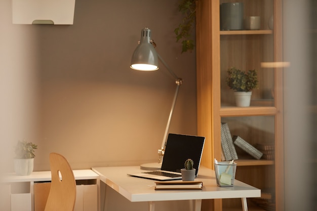 Background image of cozy home office workplace with lit desk lamp in minimal design, copy space