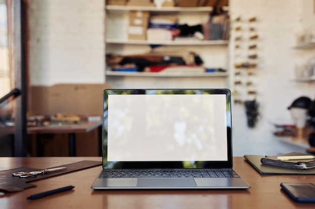 Background image of opened laptop with blank screem nock up on table in workshop interior copy space