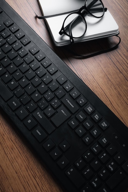 Background image of wood vintage desk focused on keyboard with notepad and glasses. Workplace.