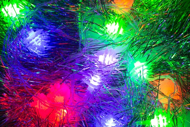 Background multicolored festive Christmas garlands glowing in the dark of night and Christmas tinsel