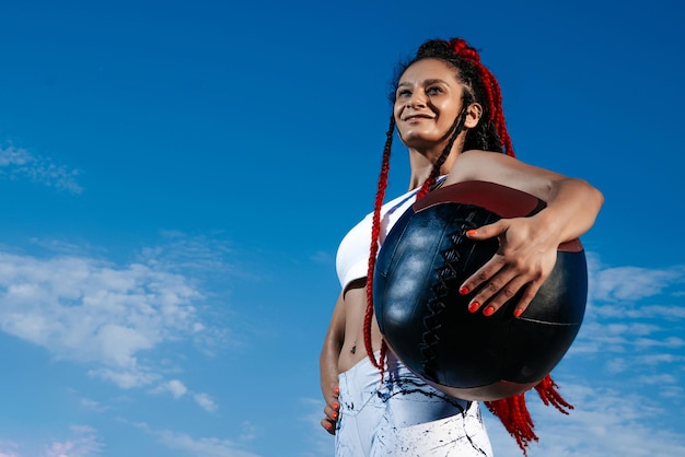 Background sky Athletic woman with med ball Strength and motivationPhoto of sporty woman in fashionable sportswear