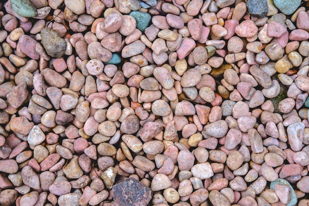 A background of small stones of a pinkish-colored shade with smooth sides and dark blotches. Top view of randomly scattered items.