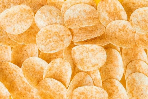 Background and texture of a heap of rotating potato chips on yellow background View from above