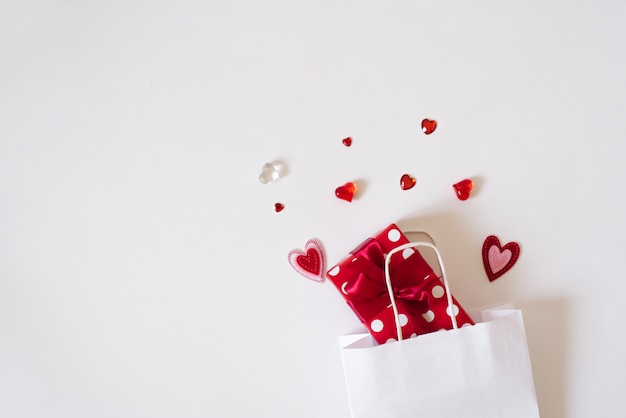 The background of Valentine's day. White paper bag, red hearts and gift on white background