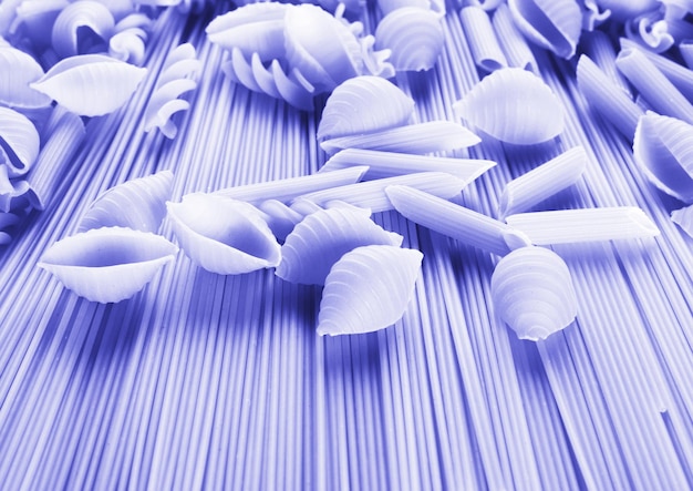 Background of wheat spaghetti and pasta of different shapes tinted in trendy color of 2022 very peri