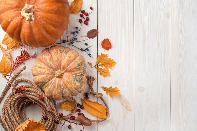 Background with autumn holiday decor Pumpkins and autumn foliage on a wooden white background