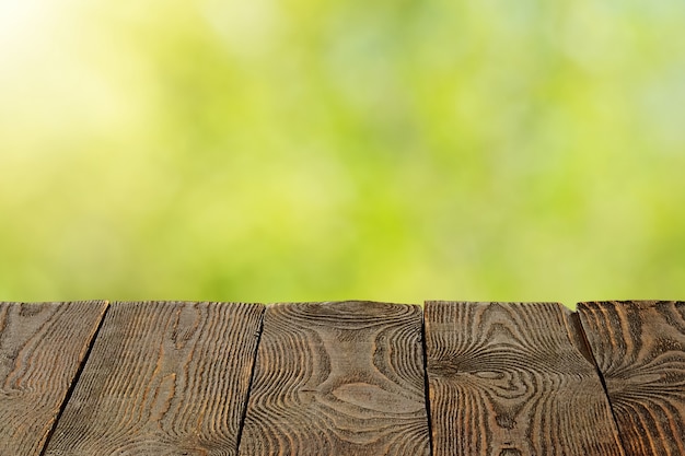 Background with blurred green leaves and empty wooden planks in the foreground