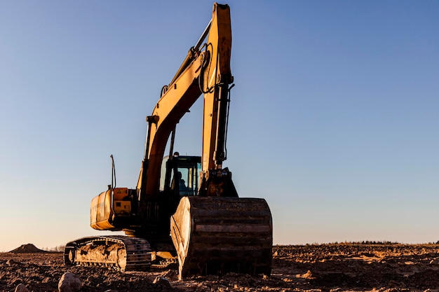 Backlit excavator on an industrial site against the background of the evening sky. Construction machinery for earthworks.