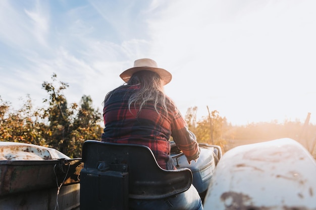 Backlit shot of a latin farmer woman driving an old tractor, in the middle of his farmland at sunset