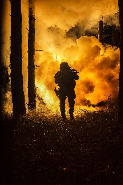 Backlit silhouette of special forces marine operator in forest on fire explosion background. Battle, bombs exploding, fighting no matter what