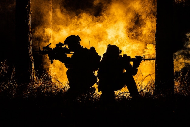 Backlit silhouette of special forces marine operators in forest on fire explosion background. Battle, bombs exploding, they fighting no matter what