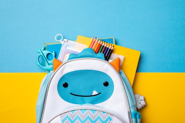 Backpack with school supplies on a blue and yellow background View from above copy space Back to school concept