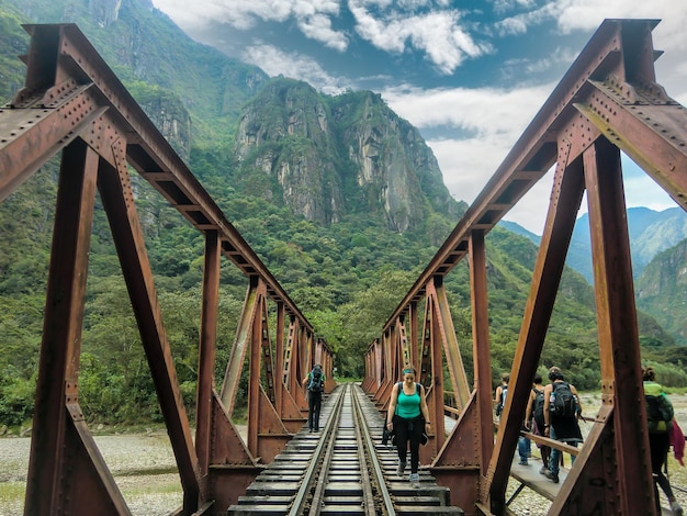 Backpackers walking along the train tracks on a metal bridge on the way to Machu Picchu, Peru.