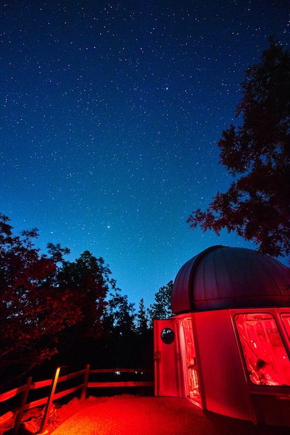 Backside of an observatory lit in red lights at night with trees in the background ominous