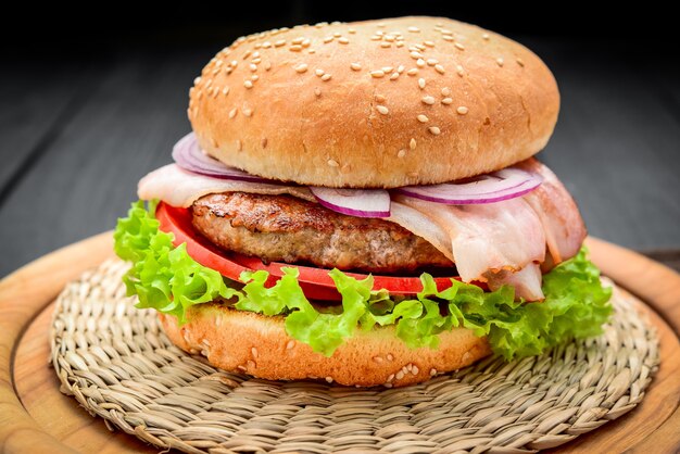 Bacon burger with beef cutlet, with fresh vegetables, on wooden background