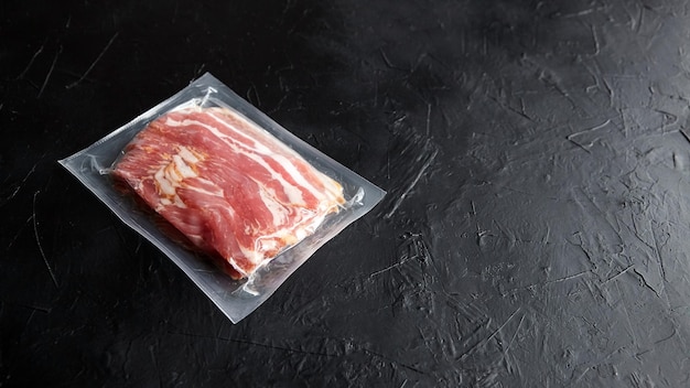 Bacon strips raw smoked pork meat slices in vacuum package on black stone table