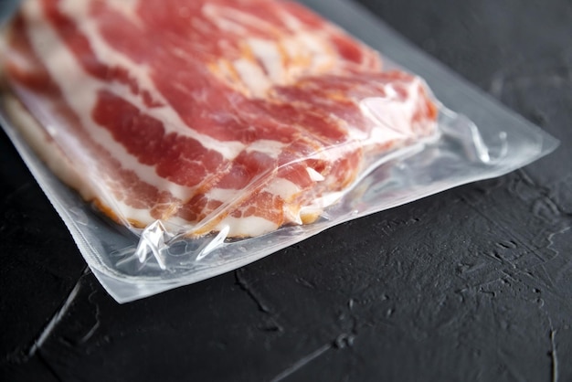 Bacon strips raw smoked pork meat slices in vacuum package on black stone table