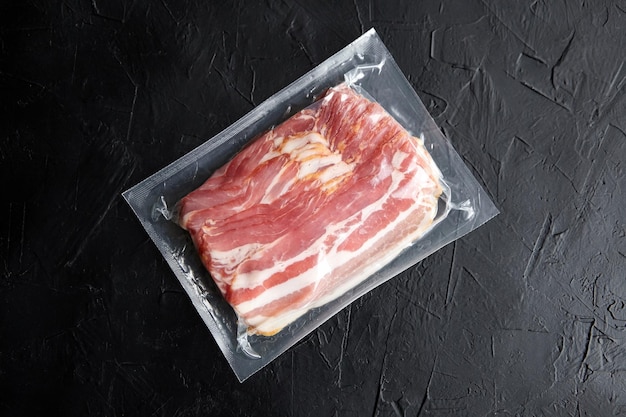 Bacon strips raw smoked pork meat slices in vacuum package on black table top view