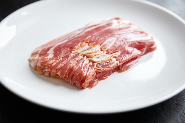 Bacon strips raw smoked pork meat slices on white plate on black table