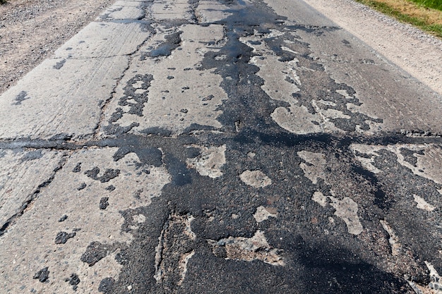 A bad asphalt road that has been repaired many times, a road of poor quality on which traffic is difficult