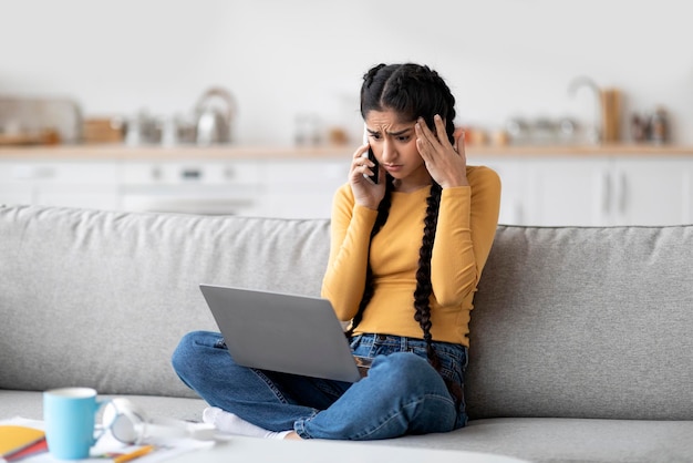 Bad news stressed indian woman looking at laptop and talking on cellphone