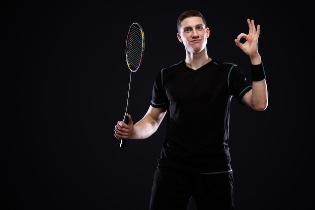 Photo badminton player in sportswear with racket and shuttlecock on black background emotional sport portrait with man which show ok and good luck