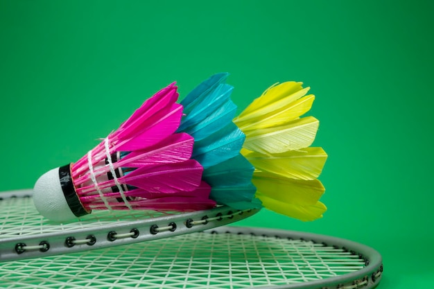 Photo badminton rackets and colorful feathered shuttlecocks in blue yellow and pink on green background