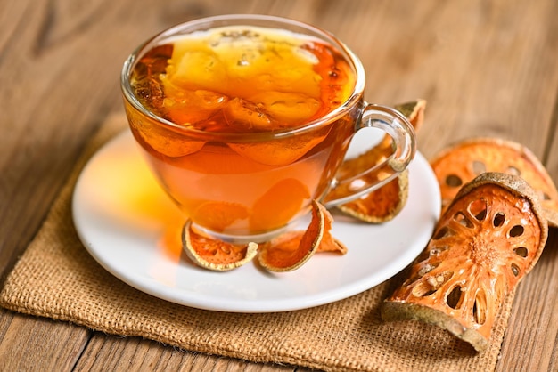 Bael tea on glass with dried bael slices on wooden background Bael juice Dry bael fruit tea for health Aegle marmelos