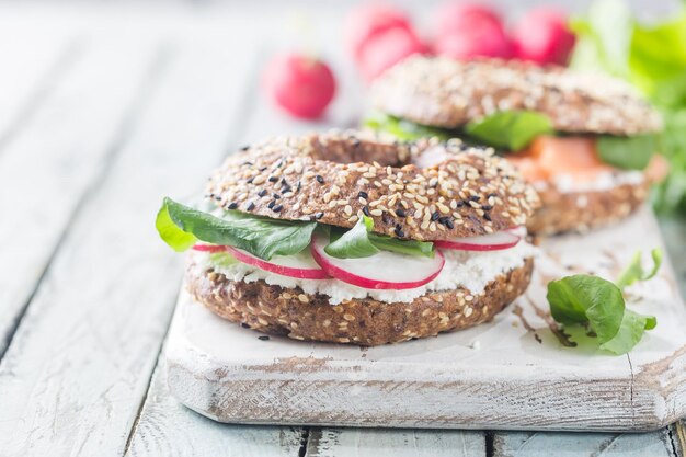 Bagels with cream cheese avocado, fish, arugula and radish on old wooden table. Healthy breakfast food.