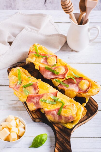 Photo baguette baked with ham cheese and basil on a wooden board vertical view