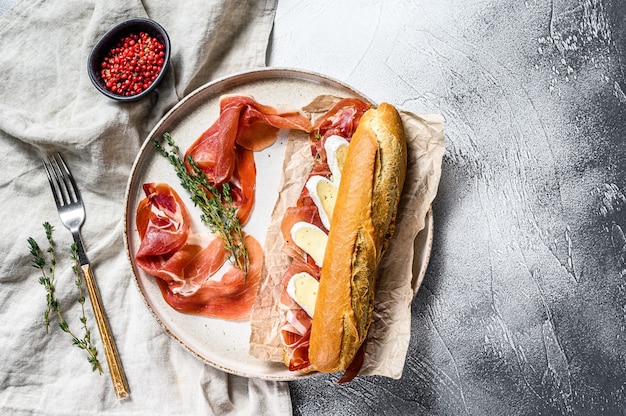 Baguette sandwich with prosciutto ham, Camembert cheese on a plate. Gray background, top view.