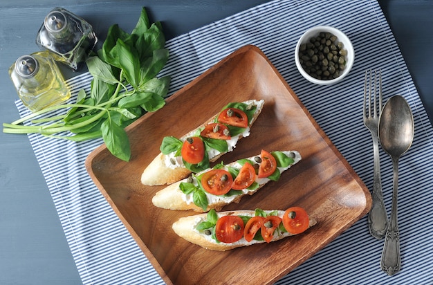 Baguette with soft cheese, basil, cherry tomatoes, capers