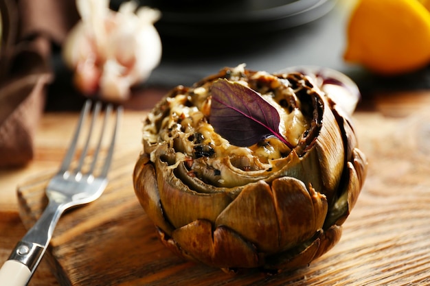 Baked artichoke on wooden cutting board close up