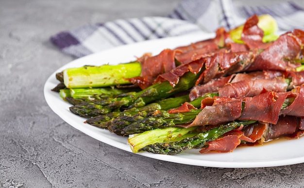 Baked asparagus with bacon and herbs on wooden background