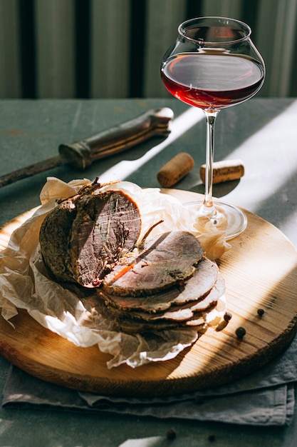 Baked boiled pork with garlic and spices with red wine in a glass on a wooden platter, gray background