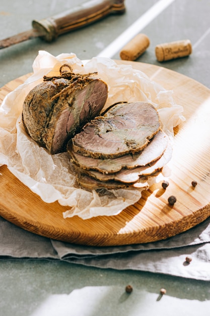 Baked boiled pork with garlic and spices on a wooden platter, gray background