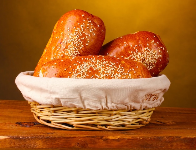 Baked bread in basket on wooden table on brown background