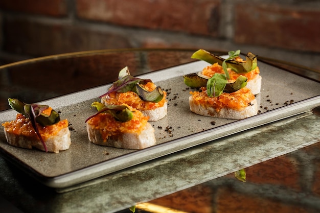 Baked bruschetta with salmon cheese sundried tomatoes and avocado in gray plate on bright background