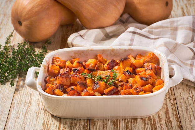 Baked butternut squash cubes with thyme on a on a white wooden table