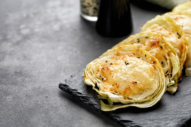 Baked cabbage pieces roasted cabbage steaks with cheese on slate board and dark background