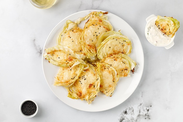 Baked cabbage pieces roasted cabbage steaks with cheese on white plate and marble background Vegan