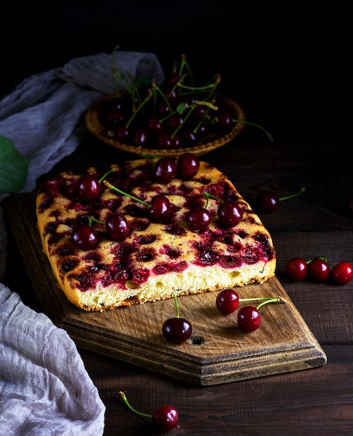 Baked cake with cherries on a brown wooden board